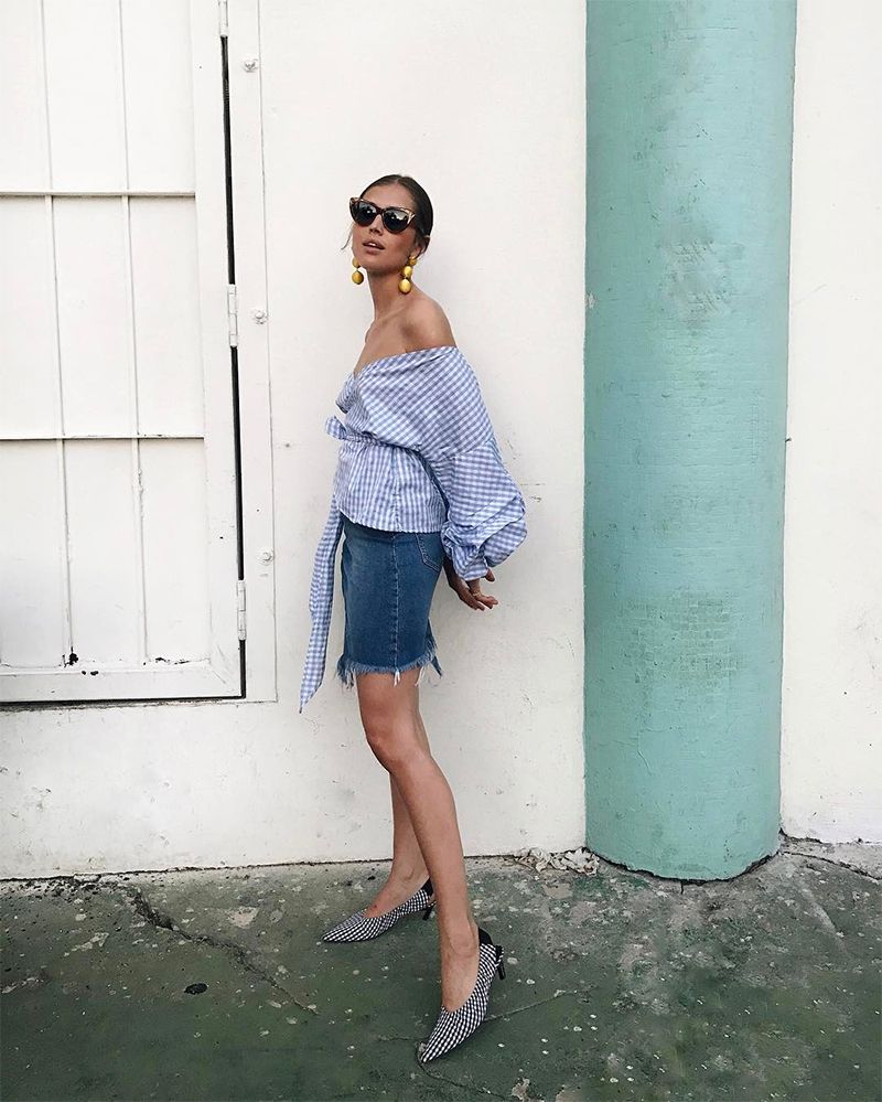 A blue denim skirt, a blue off the shoulder gingham blouse with puff sleeves, gingham shoes and statement earrings