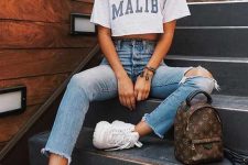 a casual look with a cropped tee, blue ripped jeans, white trainers and a brown printed backpack
