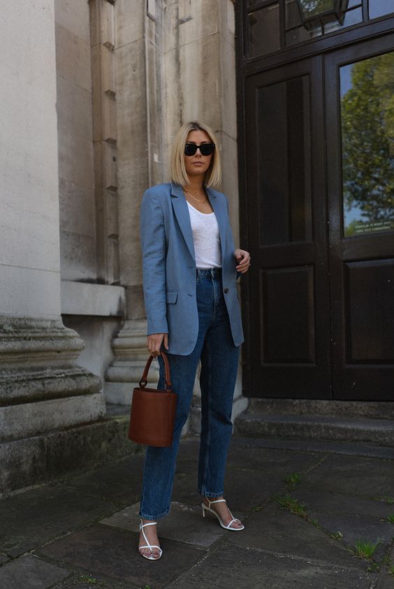 a chic summer look with a white top, blue high waisted jeans, a coastal blue blazer, white strappy kitten heels and a bucket bag