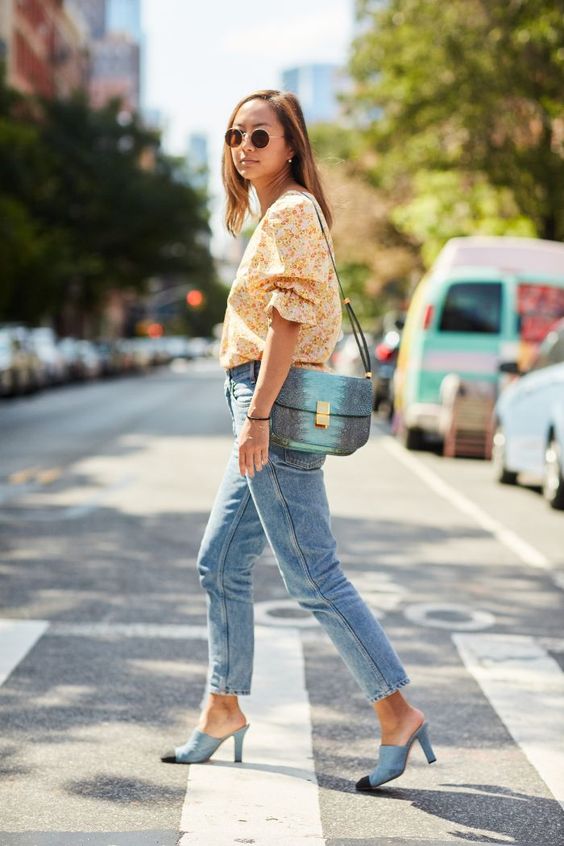 a floral printed blouse with puff sleeves, blue jeans, blue heeled mules and a blue and green bag