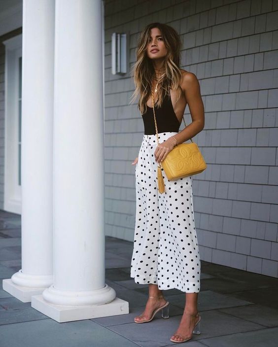 a sexy outfit with a black bodysuit with a deep neckline, white polka dot culottes, sheer heels and a yellow bag