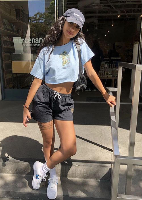 a sport chic look with a blue cropped tee, black shorts, white sneakers with socks and a black cap