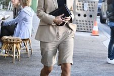 a tan short suit with a fitting blazer, Bermuda shorts, a black top and heels and a black clutch