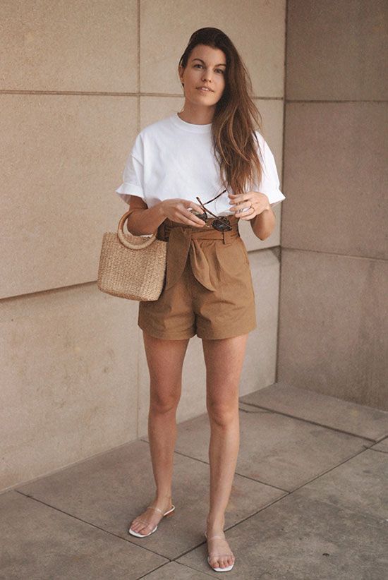 a vacation look with a white t-shirt, rust-colored paperbag waist shorts, sheer slippers and a straw bag