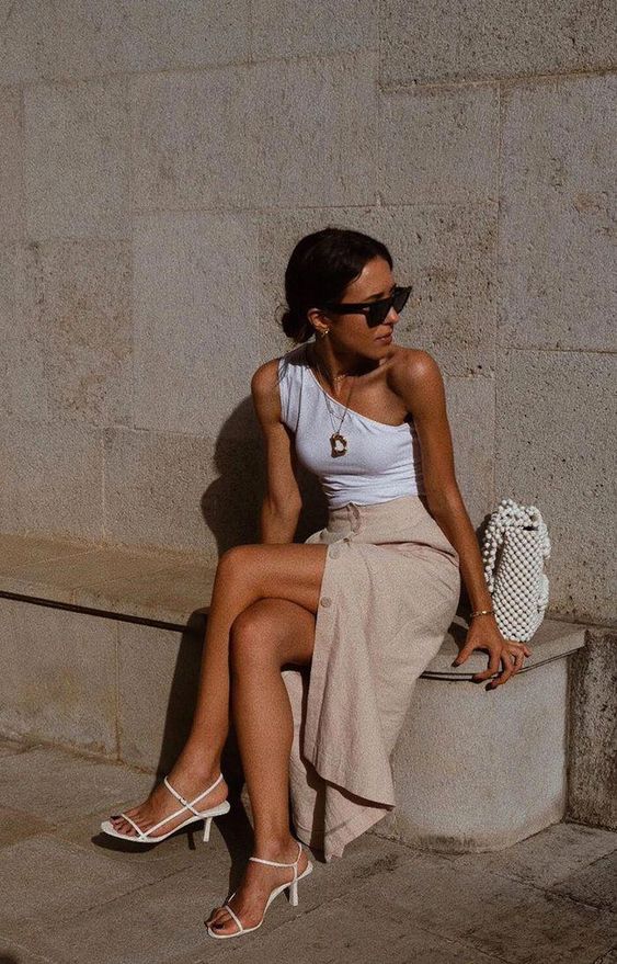 a white one shoulder top, a tan button up midi skirt, white strappy kitten heels and a beaded bag