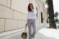 a white shirt, striped pants, red ankle strap sandals and a whimsical embellished bag