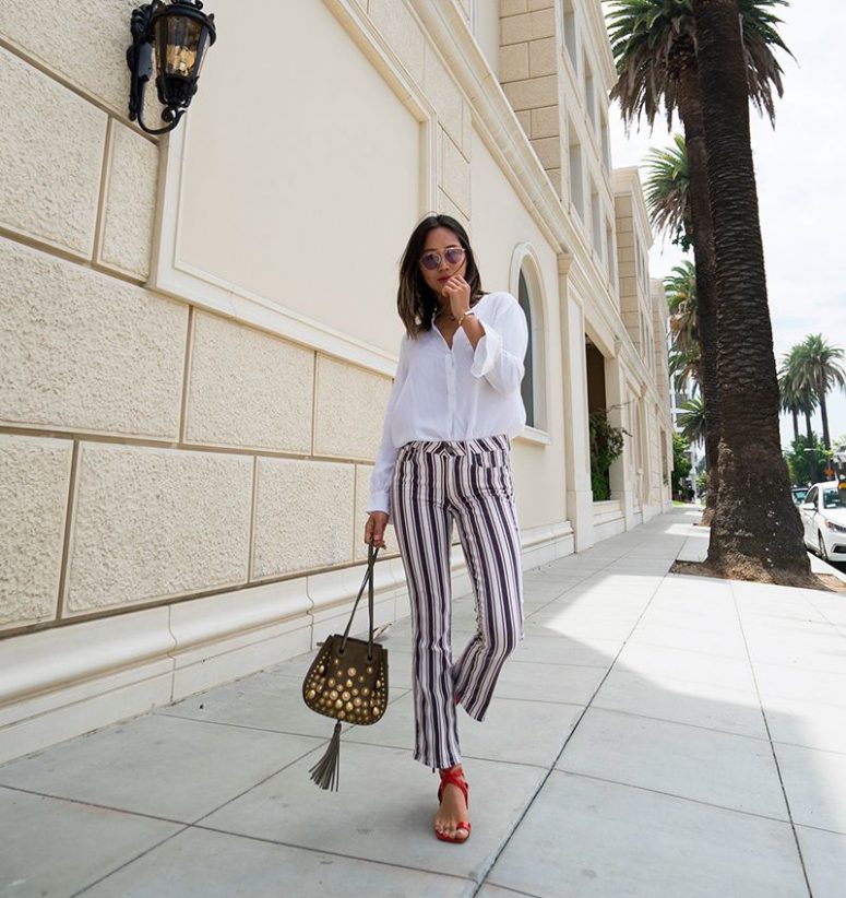 a white shirt, striped pants, red ankle strap sandals and a whimsical embellished bag