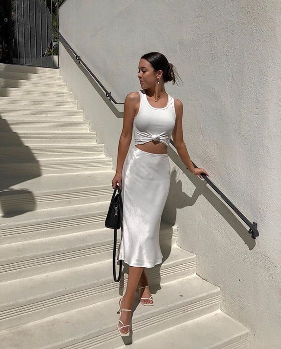 a white tied up top, a pearly slip midi skirt, white strappy kitten heels and a black bag