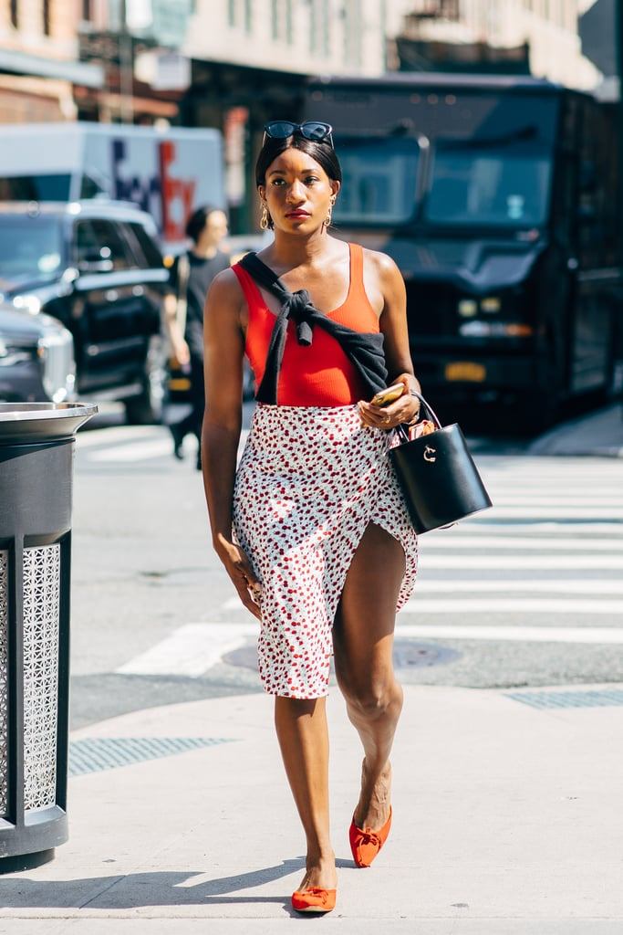 an orange top, a white and red pink dot slit midi skirt, orange mules and a black bucket bag plus statement earrings