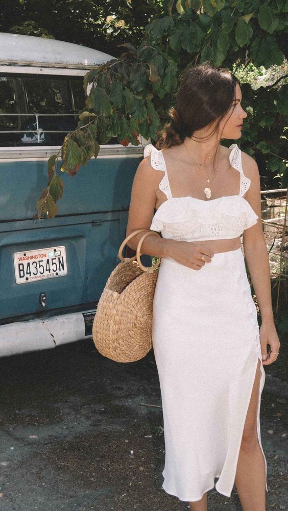 a white crochet lace crop top with ruffle straps, a high waisted midi skirt with a side slit, a round straw bag