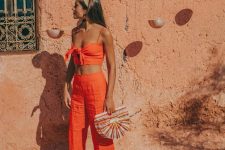 a bold orange set with trousers and a cropped tied up top, navy slippers, a bright bag