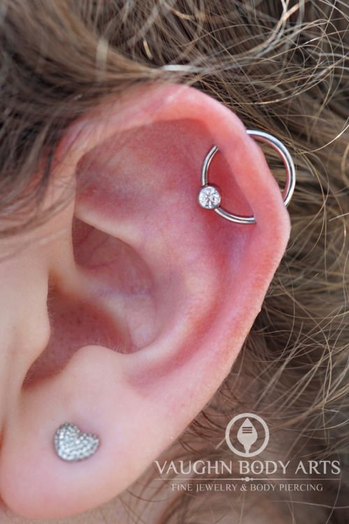 a lobe piercing paired with an orbital one, with a heart stud earring and a ring with a rhinestone are cool and bold