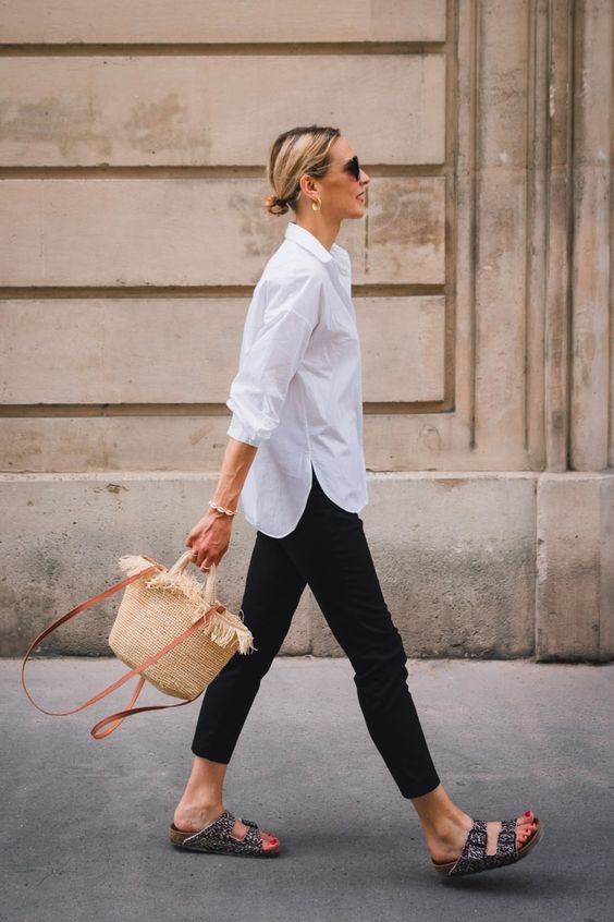 a simple look with a white shirt, black pants, printed birkenstocks and a straw bag is a cool idea