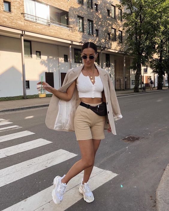 a white crop top with buttons, tan shorts, a tan oversized blazer, white trainers and a waist bag