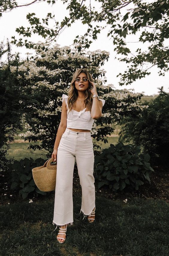 a white crop top with ruffle straps, white jeans, white strappy shoes and a straw tote
