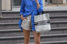 an oversized bold blue linen shirt, neutral linen shorts, flipflops and a striped shooper bag