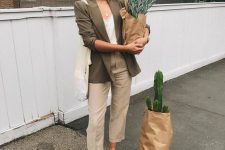 grey linen trousers, a white top, a green linen blazer, brown slippers, a neutral tote