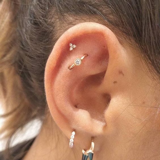 stacked ear piercings including two lobe ones, a helix and a flat orbital piercing with chic and bold earrings