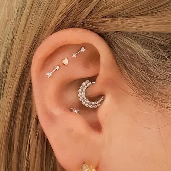 creative ear styling with a triple flat, daith, conch and lobe piercing, with heart and arrow studs and a rhinestone hoop