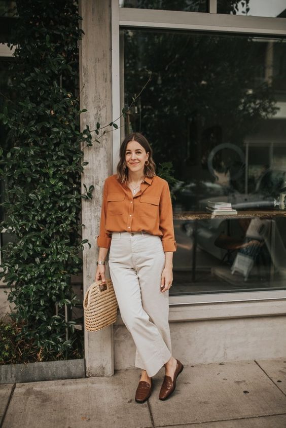 a pretty and bright outfit with a rust-colored shirt, white jeans, brown loafers, a woven bag for every day
