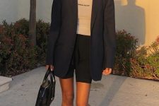 Kendall Jenner wearing a white turtleneck, black shorts, a navy oversized blazer, white boots and a black bag