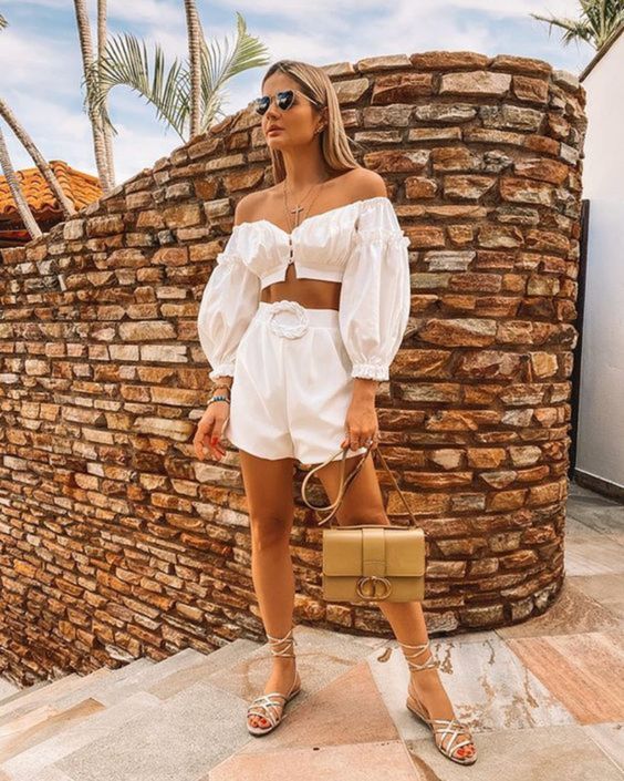 a jaw-dropping vacation outfit with a white off the shoulder puff sleeve top and high waisted shorts, strappy metallic shoes and a gold bag