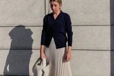a navy cardigan, a creamy pleated midi, grey trainers, a creamy bucket bag for a chic and feminine look