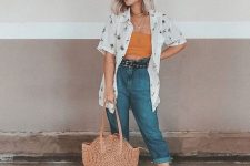 a pretty summer look with a yellow crop top, blue jeans, a white printed shirt, a woven round bag and white sandals