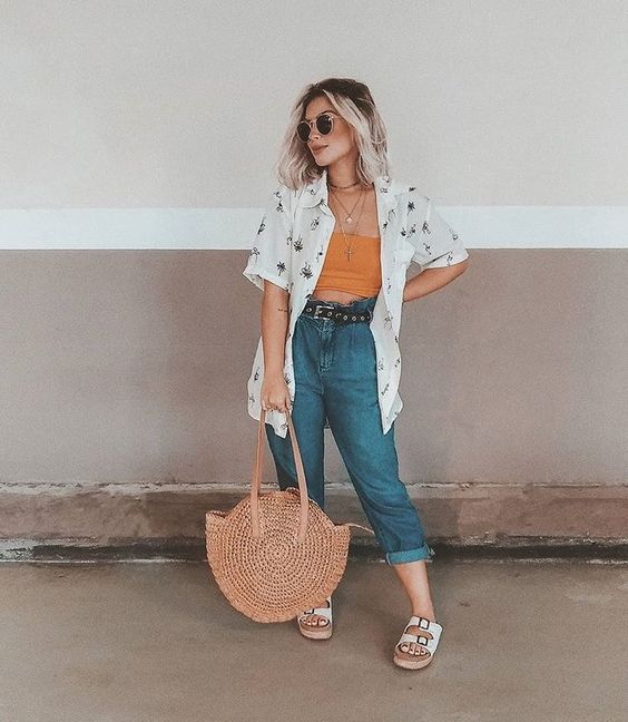 a pretty summer look with a yellow crop top, blue jeans, a white printed shirt, a woven round bag and white sandals