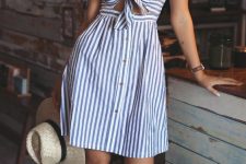 a striped blue and white summer over the knee sundress with a cutout on the front, a tied up bodice, buttons, white sneakers and a straw hat