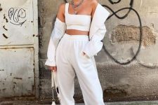a total white look with a one shoulder crop top, sweatpants, trainers, a shirt and a small bag