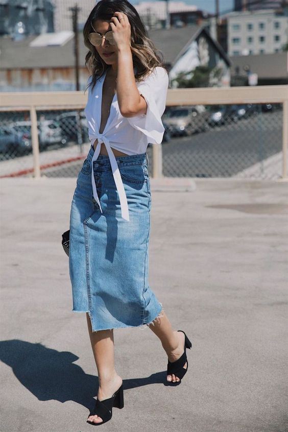 A white tied up crop top, a blue denim asymmetrical midi, black heeled mules and a wooden bag make up a cool outfit for August