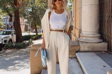 a white top, creamy trousers, a brown belt and heels, a creamy jumper and a blue bag for an effortlessly chic look