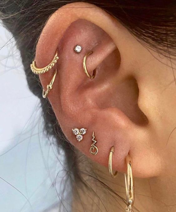bold ear styling with multiple lobe and a double helix piercing plus a rook and a flat piercing all done with gold hoops and studs