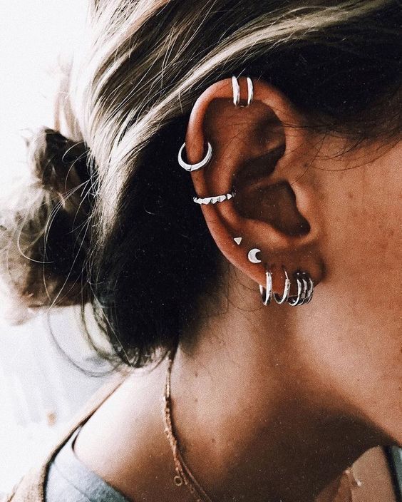 bold ear styling with stacked lobe piercings, sexeral helix ones and an upper conch piercing done with hoops and cool studs
