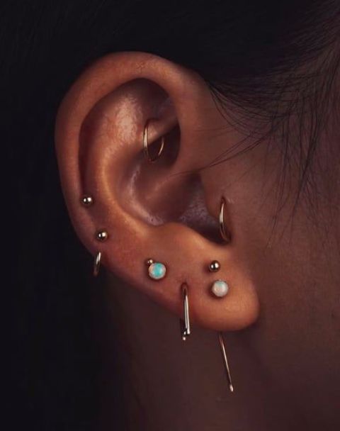 creative ear styling with a stacked lobe piercing, several helix, a tragus and a rook one with gold hoops and studs plus opal sruds