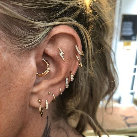 multiple stacked piercings with lobe, helix, flat and daith piercings done with gold studs and hoops