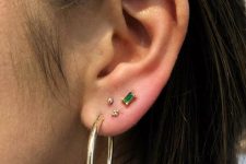 stacked lobe piercings with gold and emerald studs and a gold hoop earring for a bold and chic look
