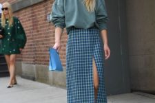 18 an oversized olive green sweatshirt, a blue plaid midi skirt wiht a front slit, blue lace up shoes and a blue clutch