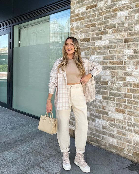a casual outfit wiht a tan crop top, neutral high waisted jeans, a plaid shirt, tan sneakers and a tan bag