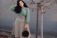 a feminine fall work outfit with a greey sweatshirt, a plaid midi A-line skirt, tan shoes and a black round bag