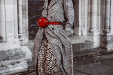 a leopard print maxi skirt, a black turtleneck, a plaid grey trench, grey trainers, a red waist bag and a black cap