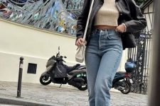 a neutral crop top, blue jeans, a black leather jacket, brown suede boots and a cream crossbody bag