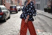 a polka dot outfit with a black top with puff sleeves, rust-colored wide leg trousers, an orange bag for summer