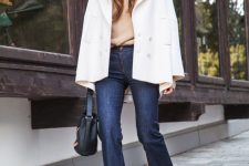 a tan sweater, navy flare jeans, a white cropped coat and a black bag for a cold fall or winter day