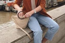 a tan t-shirt, light blue jeans, white sneakers, a rust-colored velvet blazer and a woven mini bag