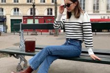 a white and black striped sweater, blue jeans, burgundy block heel boots and a matching bucket bag