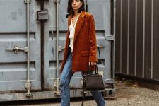 a white blouse with ruffles, an oversized rust-colored corduroy blazer, blue jeans, black heels and a black bag