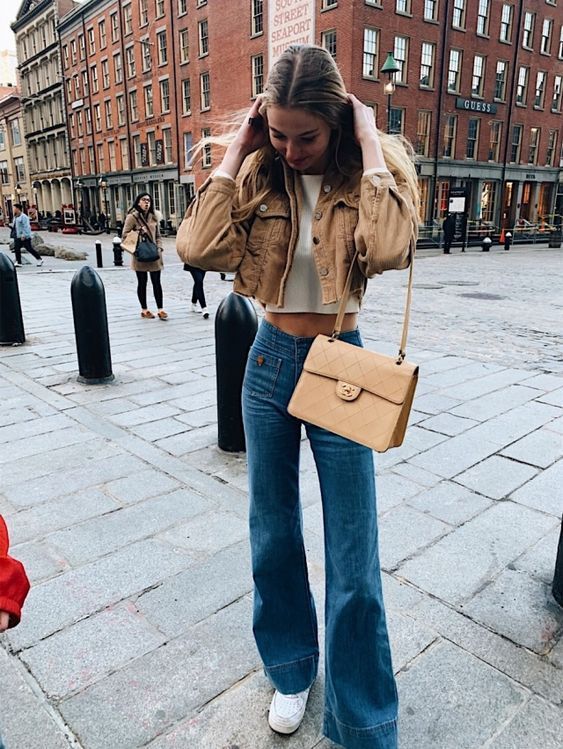 a white crop top, a brown denim cropped jacket, blue flare jeans, white trainers and a tan bag