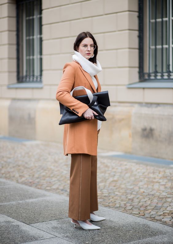 a work outfit with a white turtleneck sweater, brown trousers, white slingbacks, a rust knee coat and a black bag
